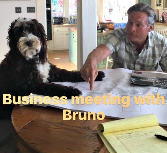 Man and dog at table looking at blueprints